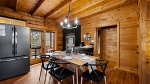 Interior de una cabaña de madera con una mesa de comedor para cuatro personas, un refrigerador, una estufa y un espejo en la pared.