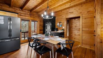 A wooden cabin interior with a dining table set for four, a refrigerator, a stove, and a mirror on the wall.