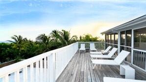 A wooden deck with white railings and lounge chairs, overlooking a tropical landscape with palm trees. - Bahama Mama 5 Bedroom Home (Governor's Harbour)