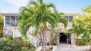 A two-story house with a stone facade, a white staircase, and a well-maintained garden with palm trees and flowering plants. - Bahama Mama 5 Bedroom Home (Governor's Harbour)