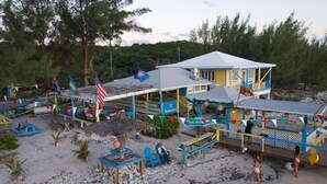 A beachside building with a Heineken sign, outdoor seating, and a thatched-roof structure.
