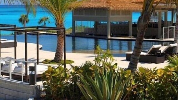 A poolside area with lounge chairs, a thatched-roof structure, and a view of the ocean.