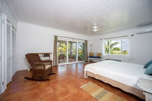 Een slaapkamer met een bed, een stoel, een raam en uitzicht op palmbomen.