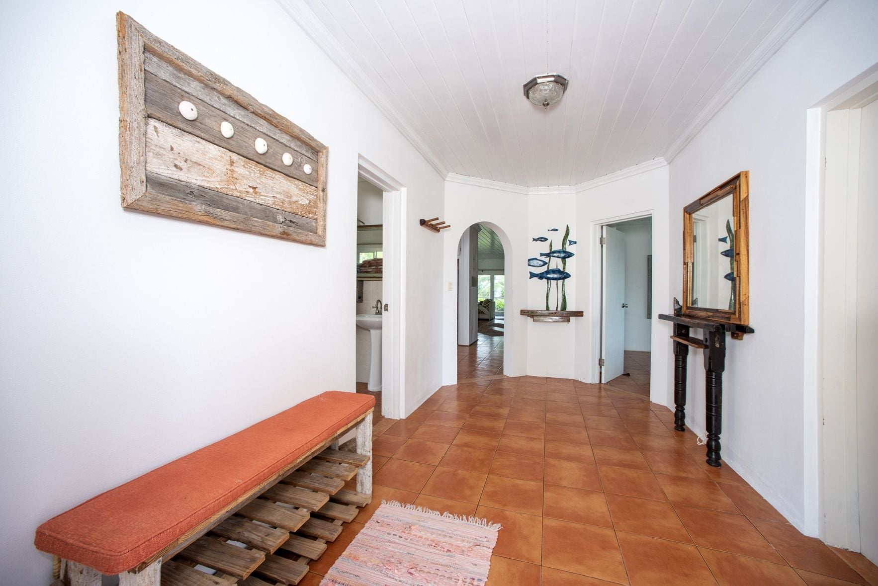 A hallway with a bench, a wall-mounted light fixture, and a mirror.