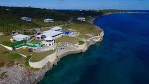 A coastal property with a large house, a swimming pool, and a cliff overlooking the ocean.