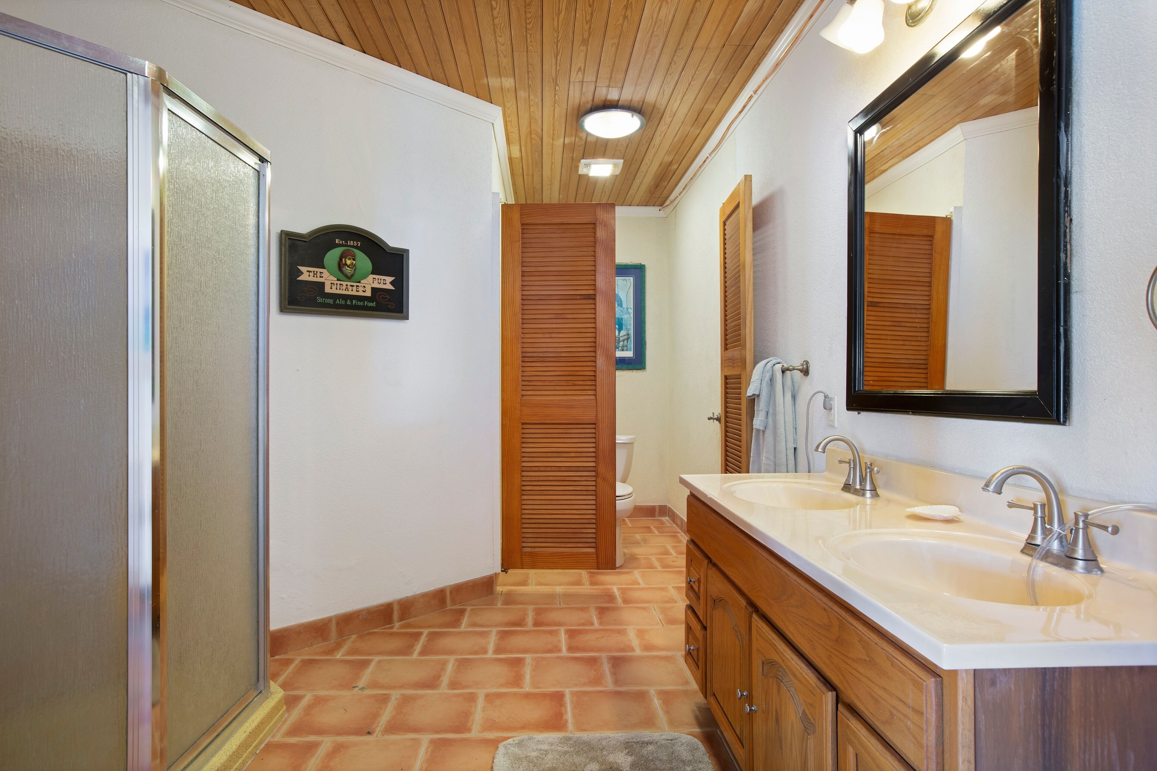 A bathroom with a wooden vanity, two sinks, a large mirror, and a toilet.