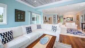 Un salón amplio con un sofá seccional blanco, una mesa de centro de madera y una alfombra azul estampada.