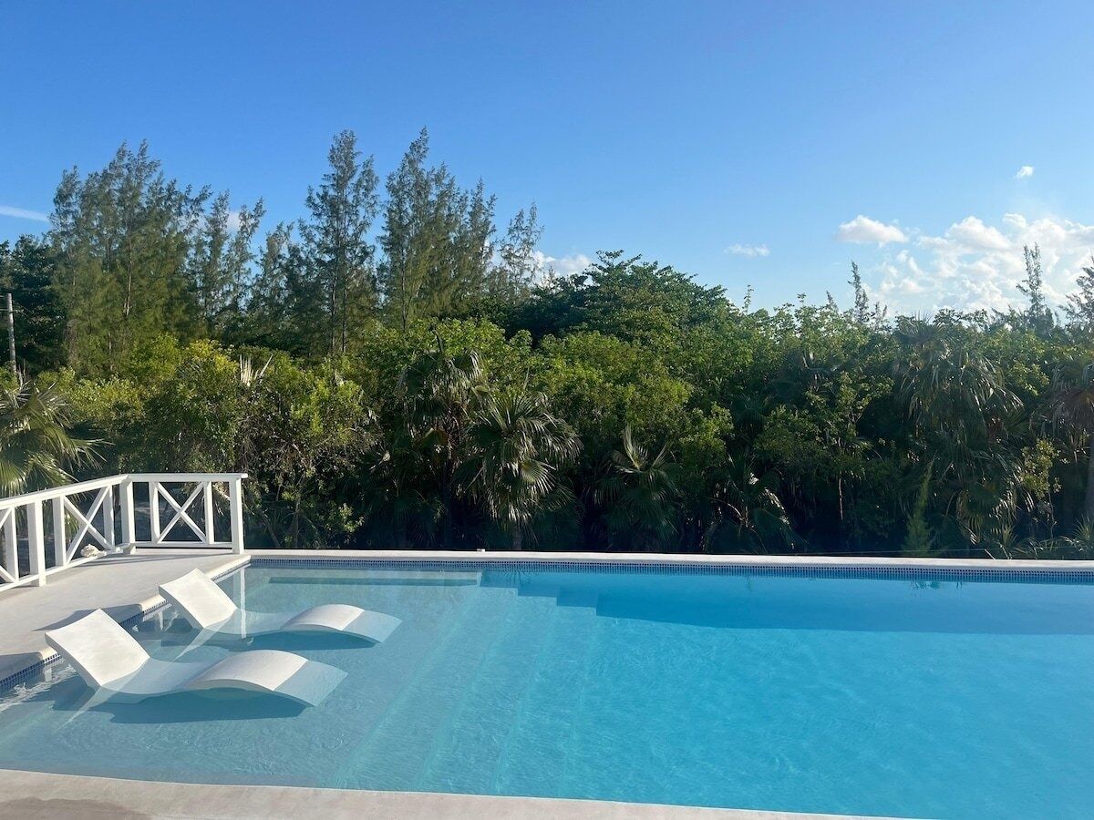Une piscine d’un bleu éclatant, bordée de chaises longues blanches et d’une terrasse également blanche.