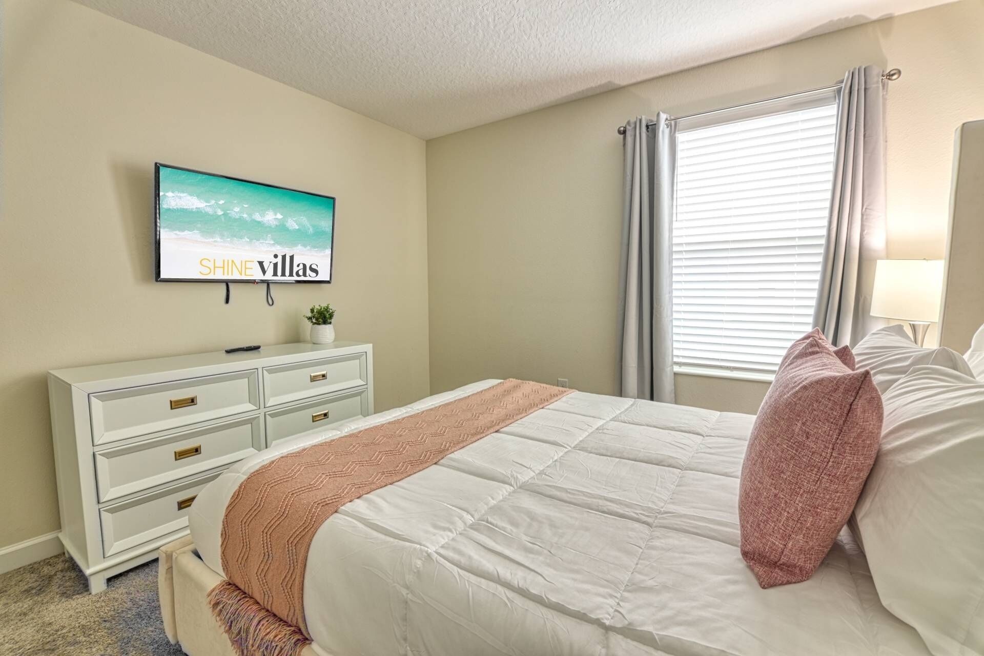 Un dormitorio con cama, cómoda, televisor y ventana con cortinas.