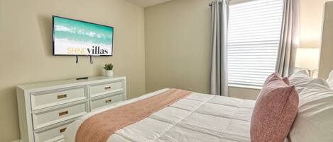 Un dormitorio con cama, cómoda, televisor y ventana con cortinas.