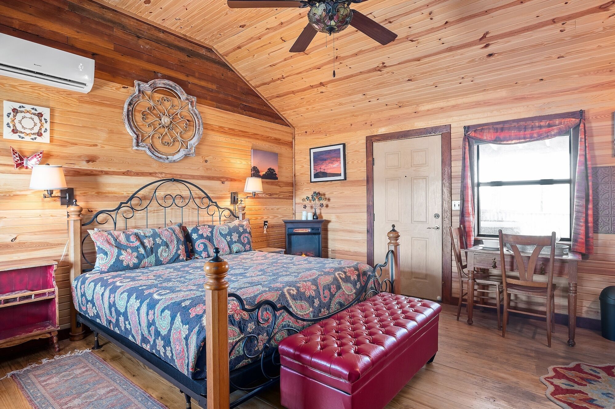 A cozy wooden room with a bed, a red bench, a table, and a ceiling fan.