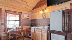 A cozy cabin-style kitchen with wooden walls, a wooden dining table, chairs, a refrigerator, a microwave, and a coffee maker.