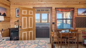 A cozy room with a bed, a wooden desk, a dining table, and a large window offering a view of the outdoors.