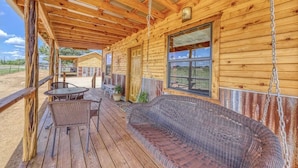 A wooden cabin with a covered porch, a wicker sofa, and a table with chairs.