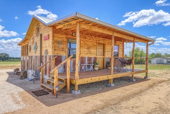 A wooden cabin with a porch, a staircase, and a small outdoor seating area.