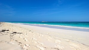 Een strand met wit zand en helderblauw water.