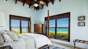 Een slaapkamer met een groot bed, een houten hoofdbord en uitzicht op de oceaan.