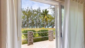 A balcony with a view of a lawn, palm tree, and distant trees. - Moonflower 4 Bedroom Home (Gregory Town)