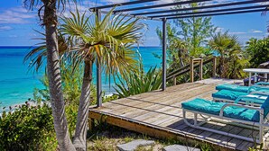 A wooden deck with lounge chairs and a view of the ocean.