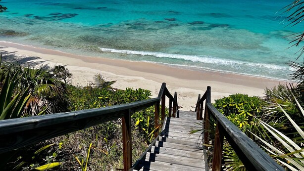 A wooden staircase leading to a beach with clear turquoise waters and a sandy shore.