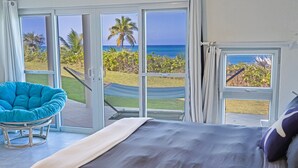 A bedroom with a bed, a blue chair, and a view of the ocean through large glass doors.
