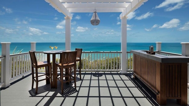 A covered outdoor area with a wooden table and chairs, a hanging light fixture, and a view of the ocean. - Buttonwood Reserve Main Lodge 1 Bedroom Home (James Cistern)