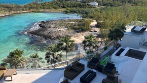 Terraza en la azotea con mobiliario de mimbre, con vistas a una zona costera de aguas turquesas cristalinas y un litoral rocoso.