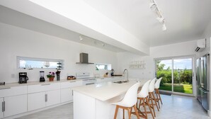 Una cocina moderna con una isla central, muebles blancos y un amplio ventanal con vistas a un jardín.