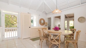 Un coin repas avec une table ronde, des chaises en bois, un ventilateur de plafond et une vue sur l’extérieur, visible à travers une porte.