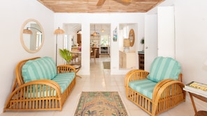 A spacious living area with wicker furniture, a kitchen in the background, and a hallway leading to other rooms.