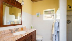 Ein Badezimmer mit Marmorwaschbecken, Holzschränken, einer weißen Toilette, einer Dusche und einem Fenster mit Blick.