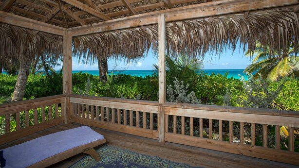 Eine Holzterrasse mit einem Reetdach, einer Bank und Blick auf das Meer.