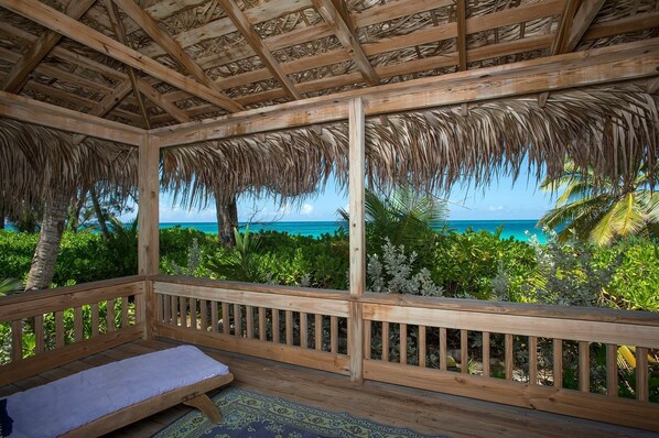A wooden deck with a thatched roof, a bench, and a view of the ocean. - Poponi House 2 Bedroom Home (North Palmetto Point)