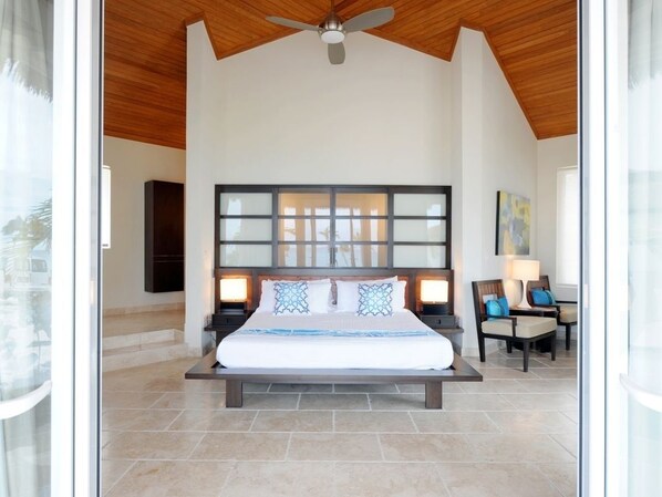 Une chambre avec un grand lit, un ventilateur de plafond et une vue sur l’extérieur, visible à travers une porte vitrée.