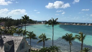 A coastal view with turquoise waters, palm trees, and a white building with a sloped roof. - Sky Beach Club Bungalow 1 Bedroom Cabin (Governor's Harbour)