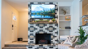 Una sala de estar con chimenea, televisor montado encima y un sofá.
