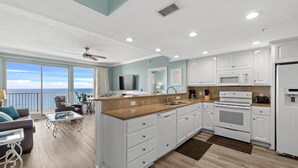 A modern kitchen with white cabinets, a granite countertop, and a view of the ocean.