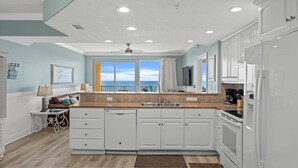 A modern kitchen with white cabinets, a large island, and a view of the ocean.