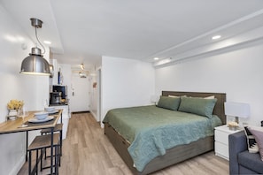 Quarto moderno com cama, mesa de cabeceira, lumin ária e pequeno espaço de escritório com cadeira e máquina de café.