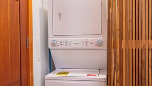 A laundry room with a stacked washer and dryer, wooden doors, and a white wall.