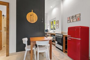 Una cocina moderna con una mesa de comedor de madera, sillas blancas, un refrigerador rojo y una pared de acento negra.