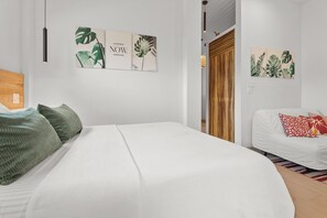 A modern bedroom with a large bed, a white sofa, and tropical-themed wall art. - Cosy brand new apartment ON the beach IN Placencia village (Placencia)