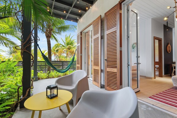 A modern outdoor seating area with a yellow table and white chairs, a hammock, and a view of palm trees.