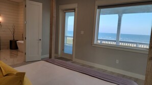 A bedroom with a large window overlooking the ocean, a bed, and a bathroom with a bathtub.