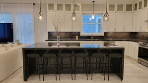 A modern kitchen with a large island, bar stools, and pendant lighting.