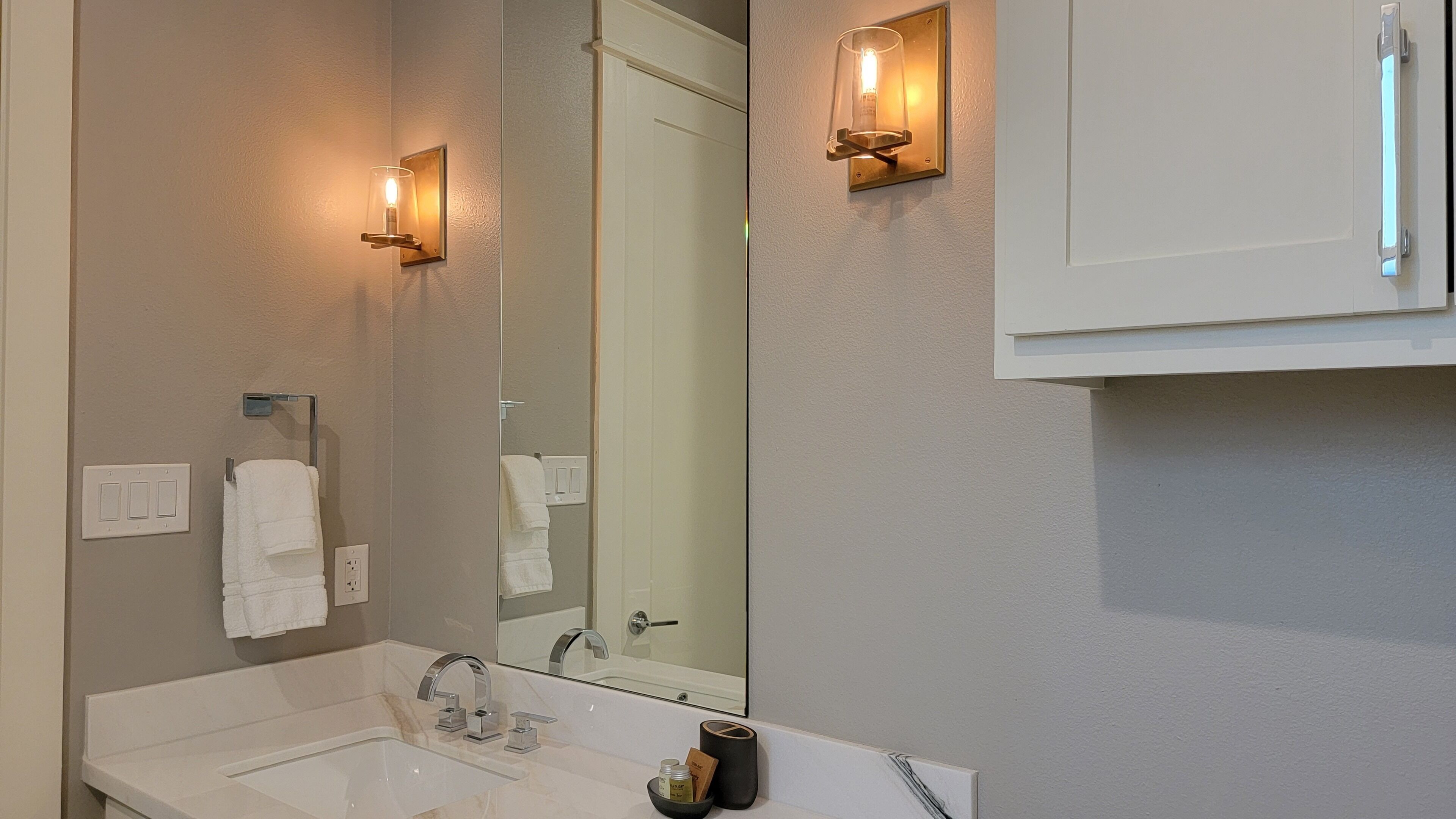 Une salle de bain avec un lavabo blanc, un miroir et deux appliques murales.