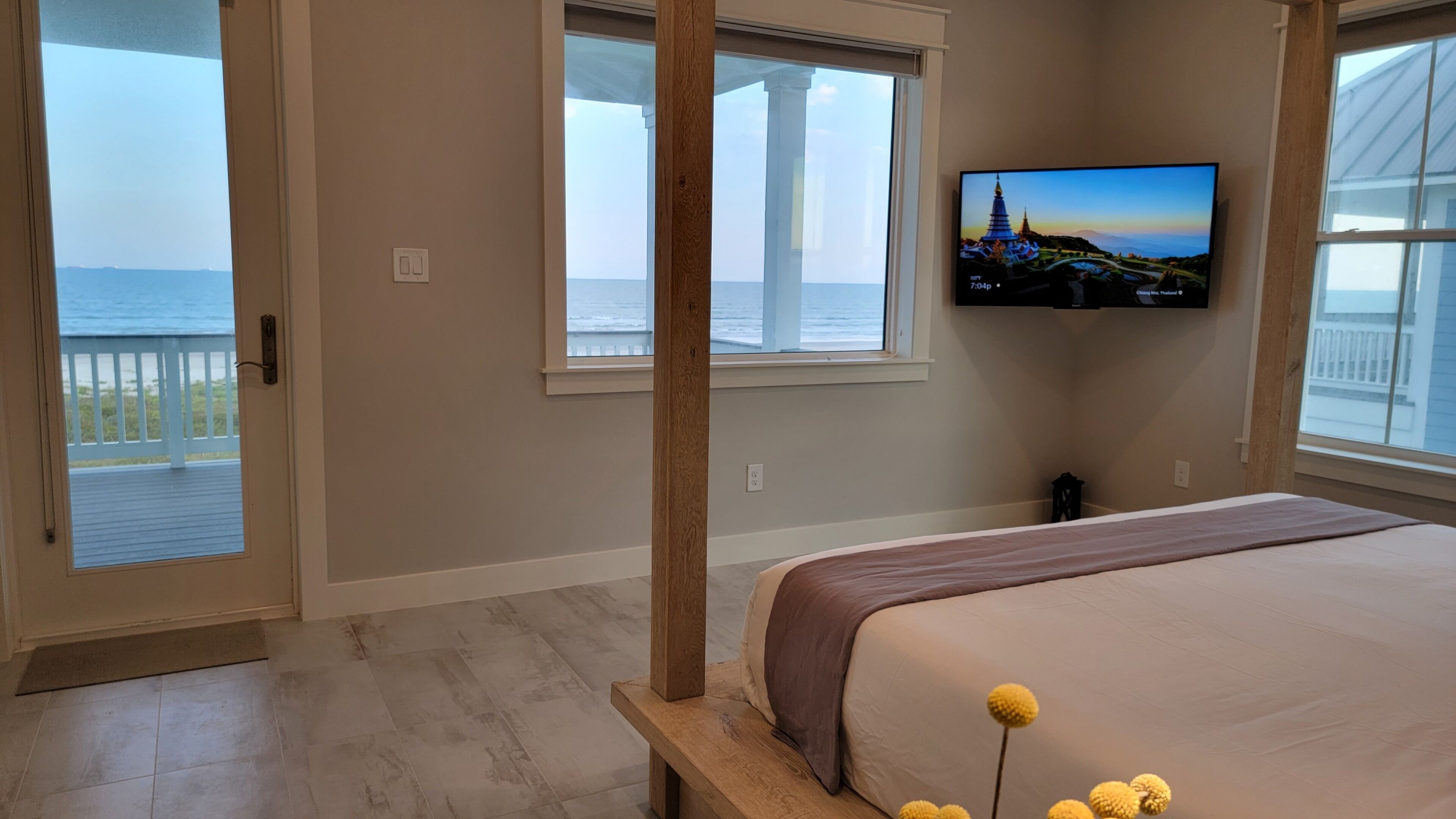 Une chambre avec un grand lit, un téléviseur fixé au mur et une vue sur l’océan par les fenêtres.