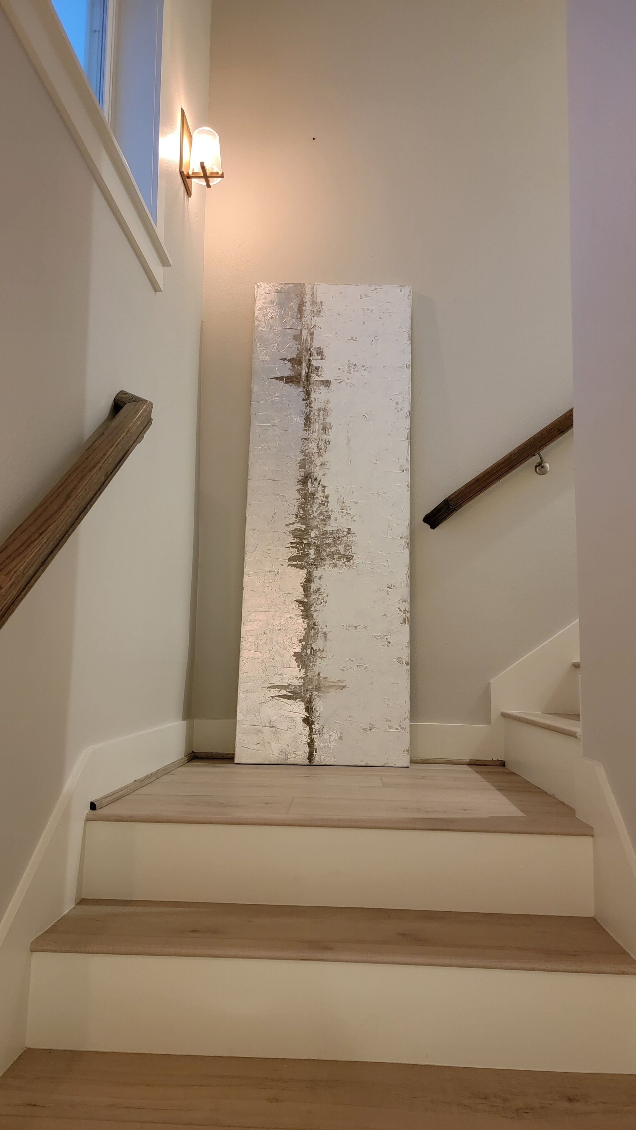 Un escalier avec des rampes en bois et une grande œuvre d’art blanche à texture marquée, située en haut.