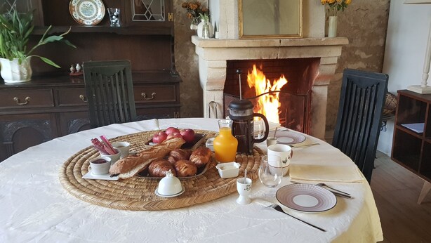 Mesa de café da manhã posta para duas pessoas, com croissants, maçãs e uma cafeteira.