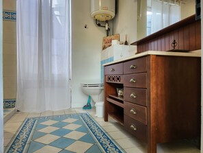 Ein Badezimmer mit Toilette, Waschbecken mit Spiegel, Holzschrank mit Schubladen und einem gemusterten Boden.